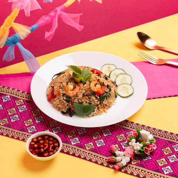 Shrimp fried rice with basil, bell peppers, and cucumber slices on a vibrant Thai-themed table.
