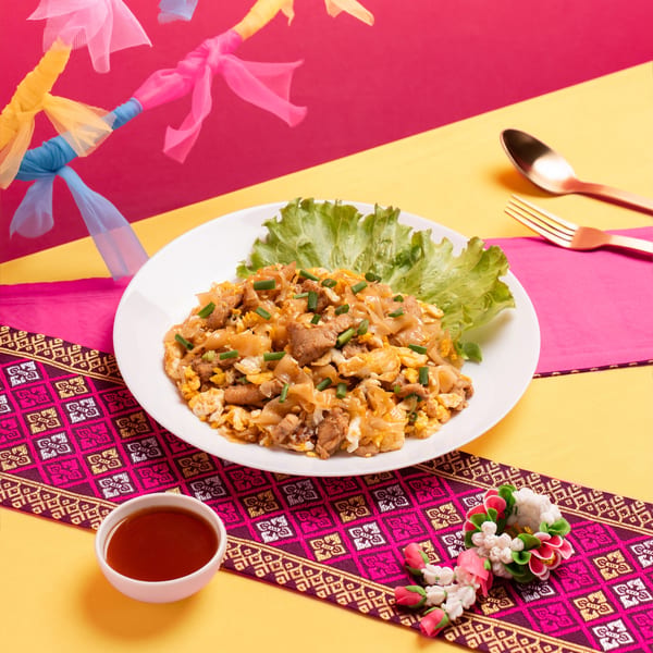 A plate of Pad See Ew with chicken and scrambled egg, garnished with lettuce and scallions.