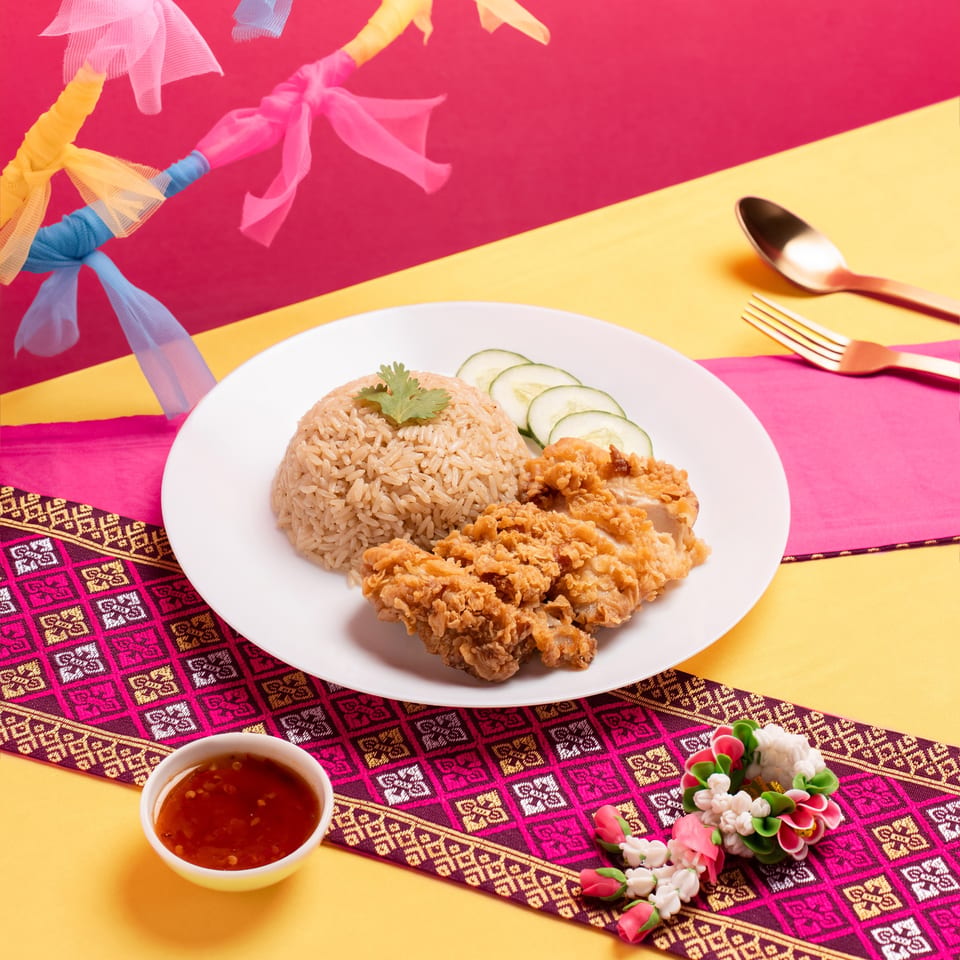 Fried chicken and rice with cucumber slices, chili sauce, and a floral garland.