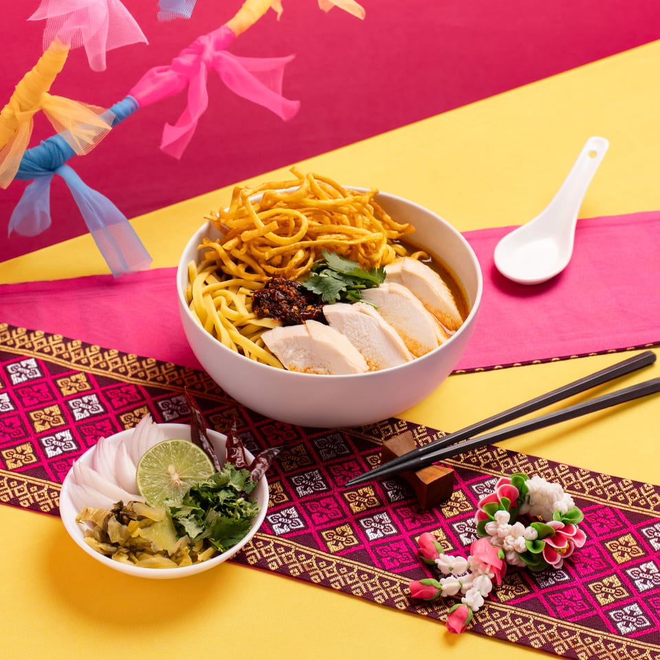Khao Soi with chicken, crispy noodles, and fresh herbs, served with chopsticks and a spoon.