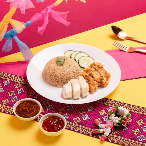 Hainanese chicken rice with fried and steamed chicken, cucumber, and two dipping sauces on a colorful background.