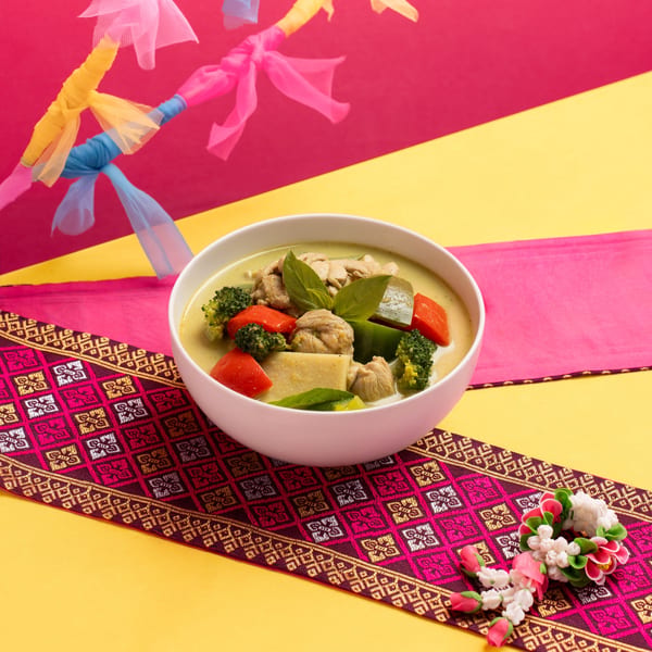 Green curry with chicken, broccoli, and peppers in a white bowl on a colorful Thai-patterned runner.