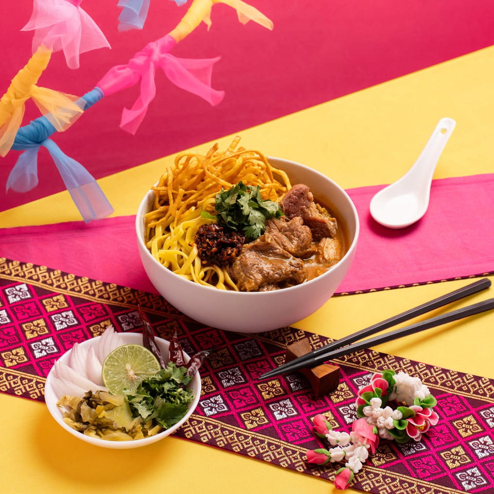Khao Soi with beef, crispy noodles, and cilantro, served with lime, onions, and pickled greens.